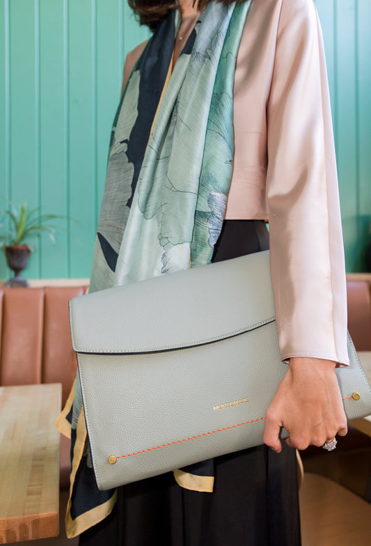 Person holding a light blue laptop case with a patterned scarf draped over their shoulder against a teal wall.