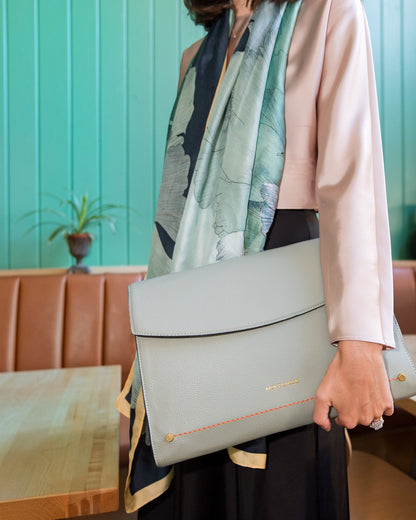Person holding a light blue laptop case with a patterned scarf draped over their shoulder against a teal wall.