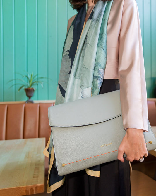 Person holding a light blue laptop case with a patterned scarf draped over their shoulder against a teal wall.