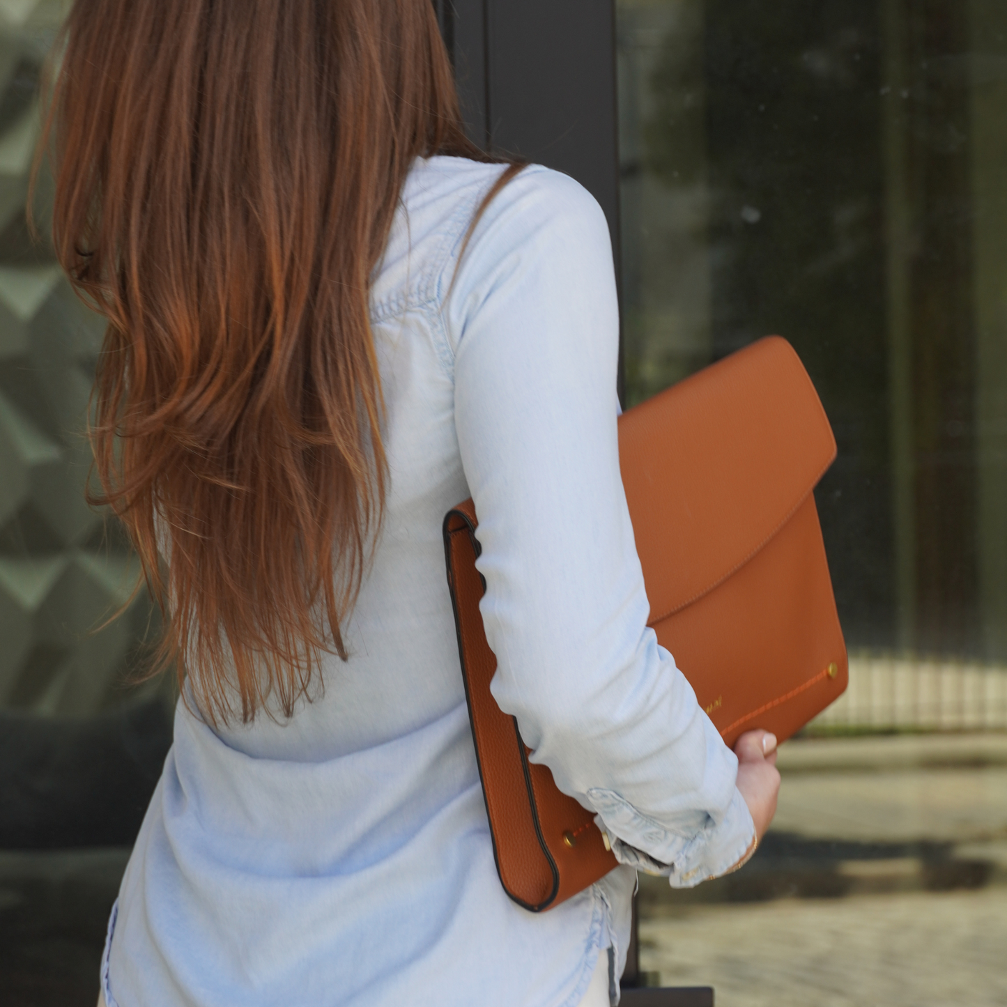 A person carrying a Montemare Vienna Laptop Case in Cognac colorway on a street