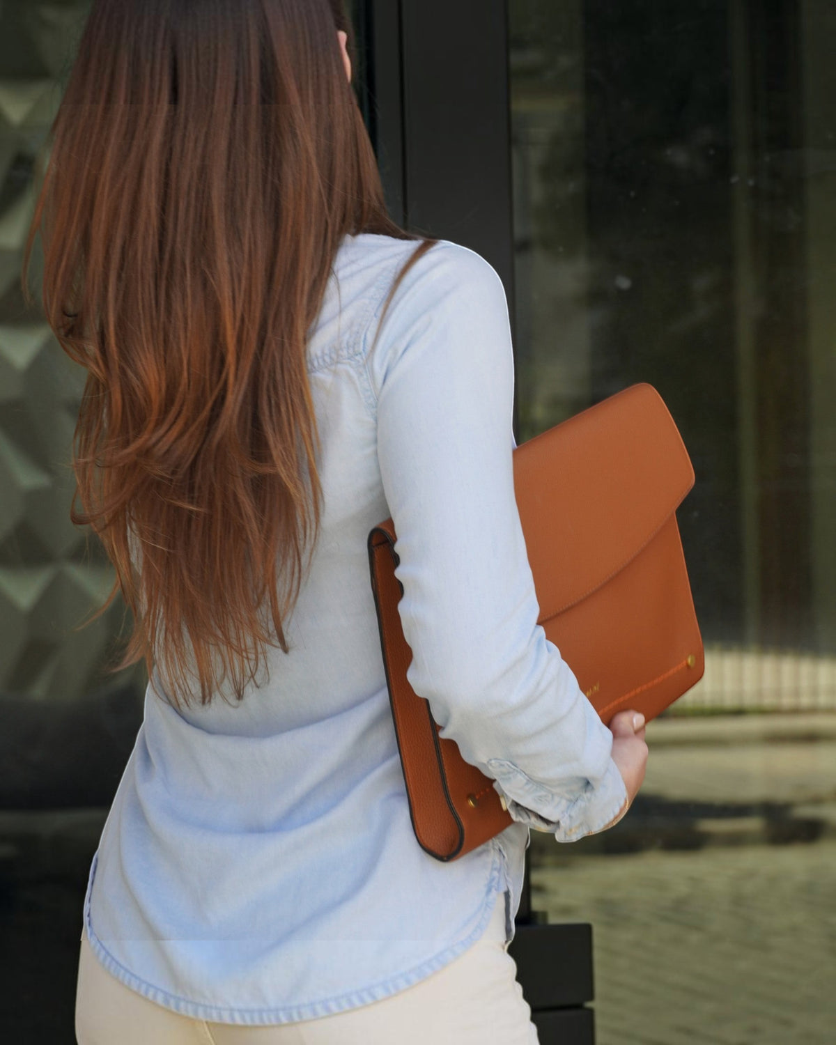 A person carrying a Montemare Vienna Laptop Case in Cognac colorway on a street