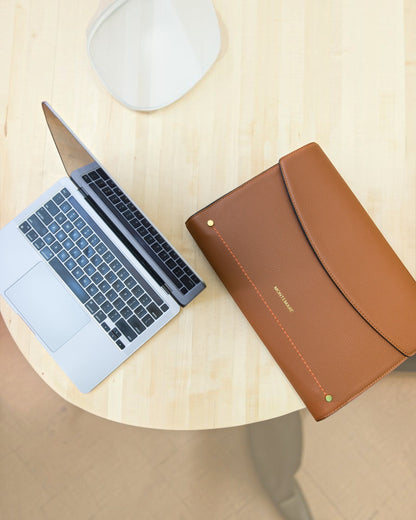 Laptop and brown leather case on a wooden surface