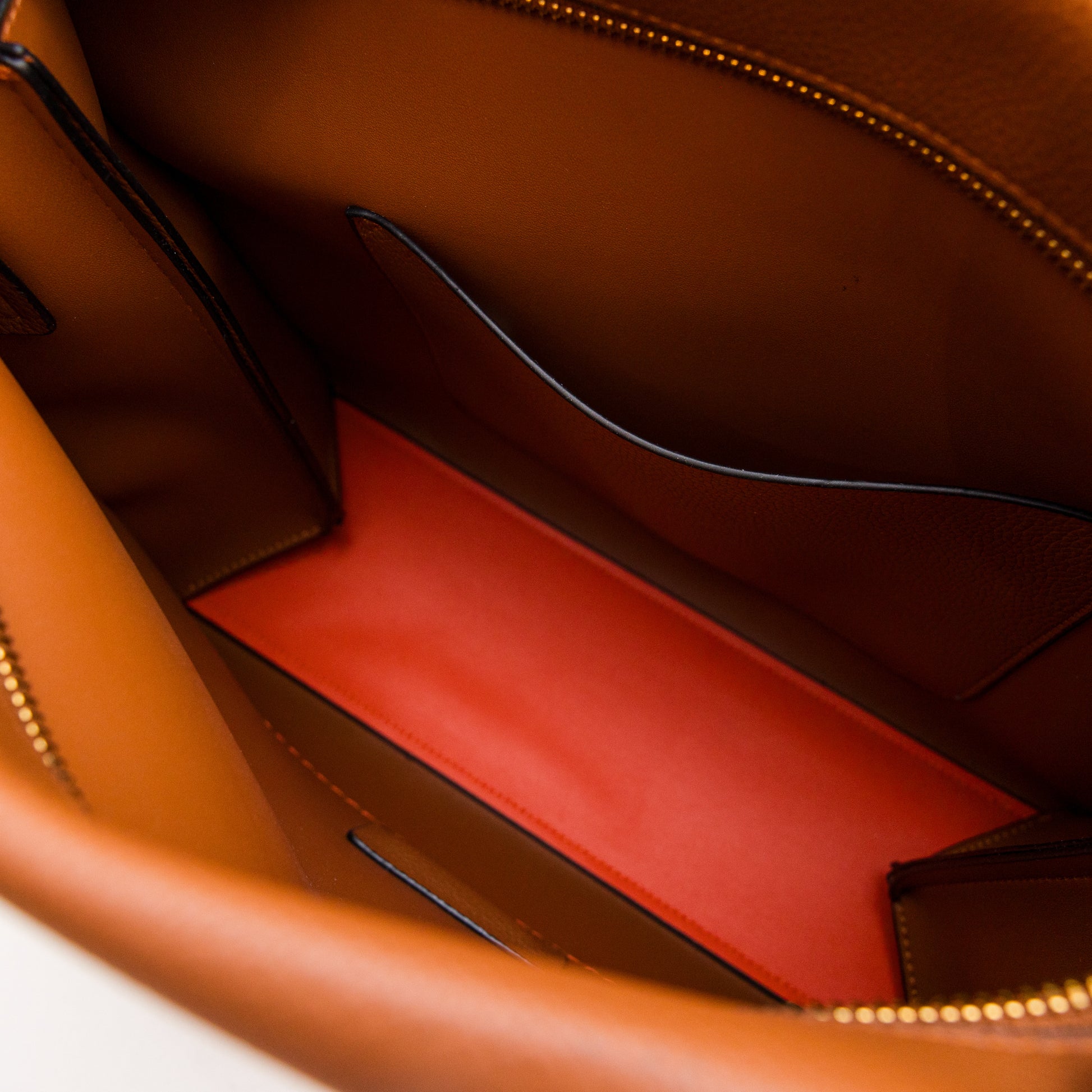 Close-up of a brown leather bag with a orange interior pocket.