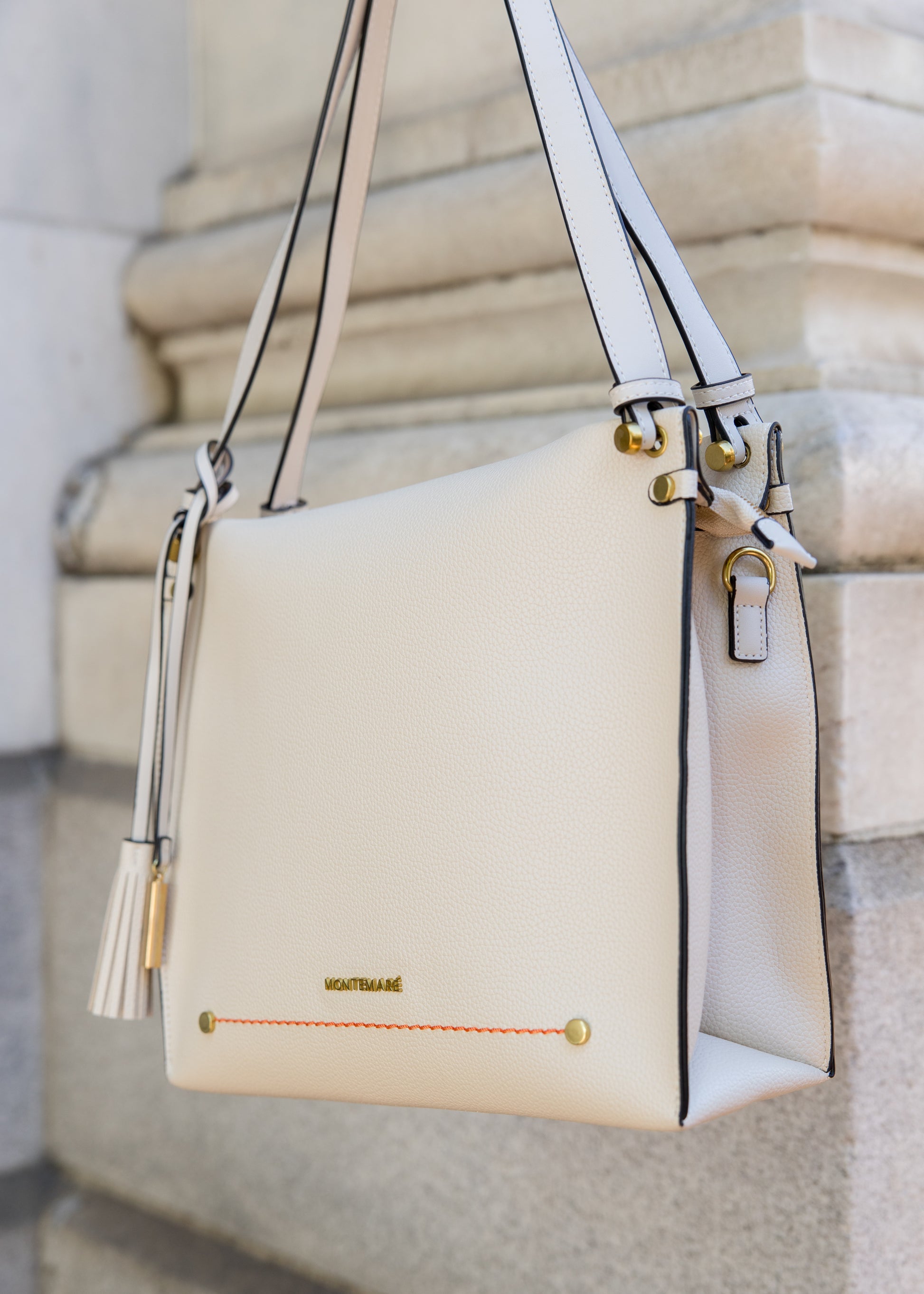 White handbag with gold accents on a stone pillar background