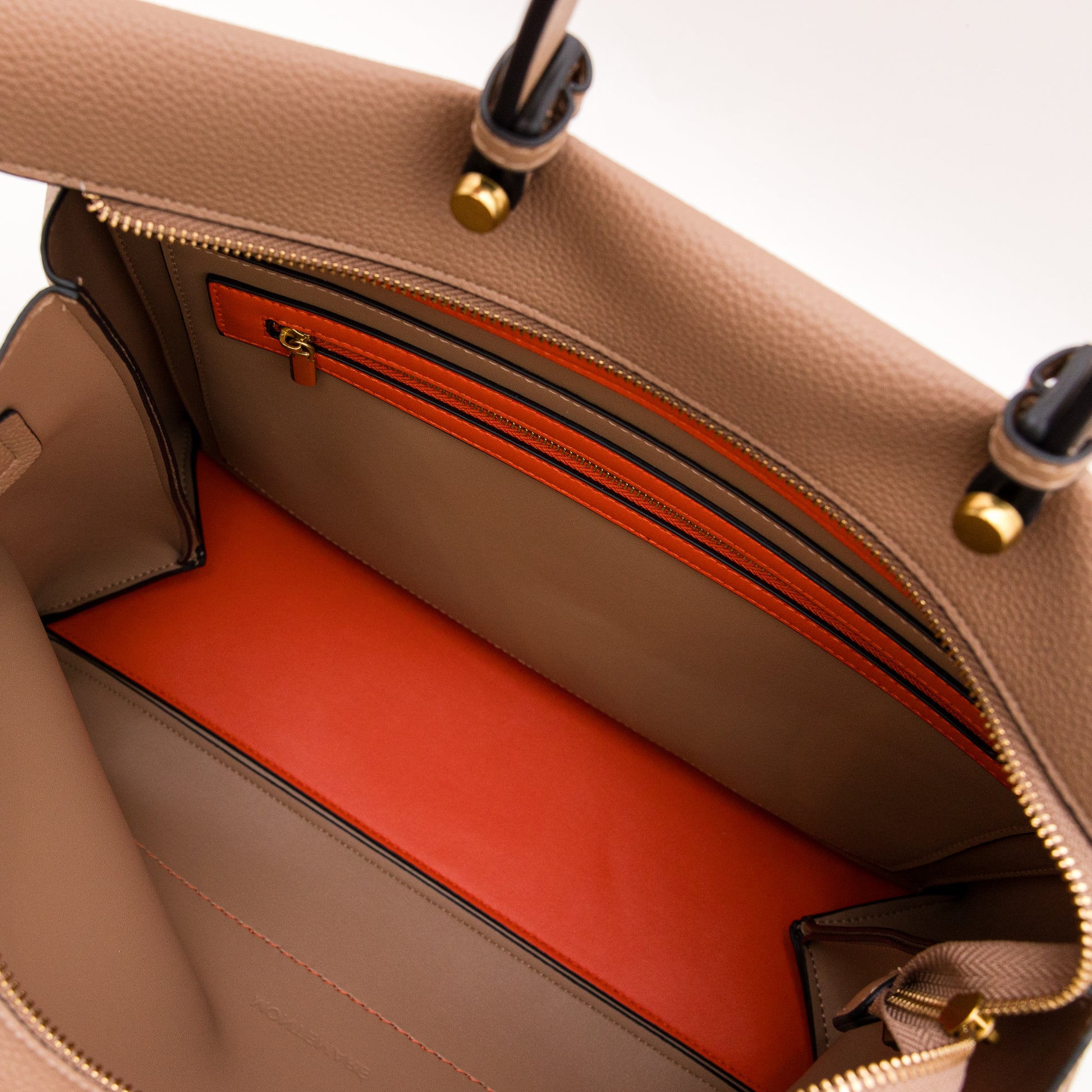 Open beige handbag with orange interior lining on a light background