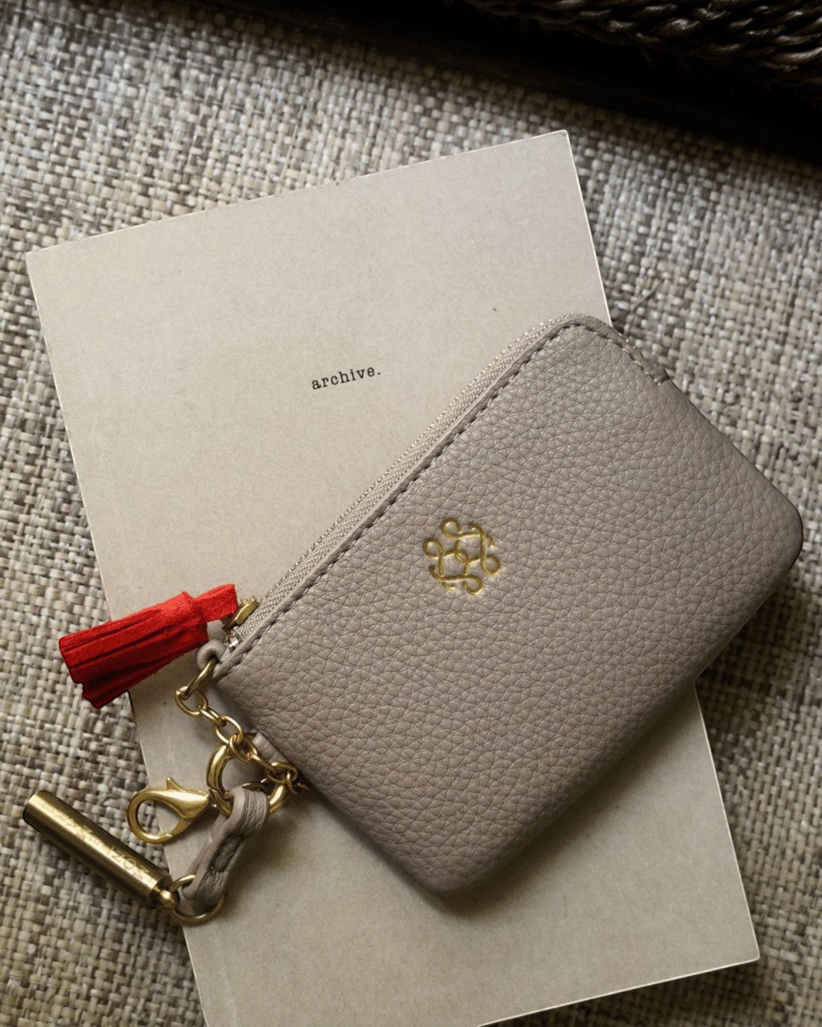 Montemaré beige vegan leather RFID card case with a gold zipper, keychain clip, and signature orange whistle tassel.