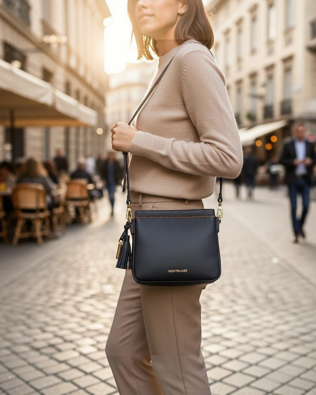 Woman wearing a black Montemaré square crossbody pouch with a tassel detail while walking on a cobblestone street.
