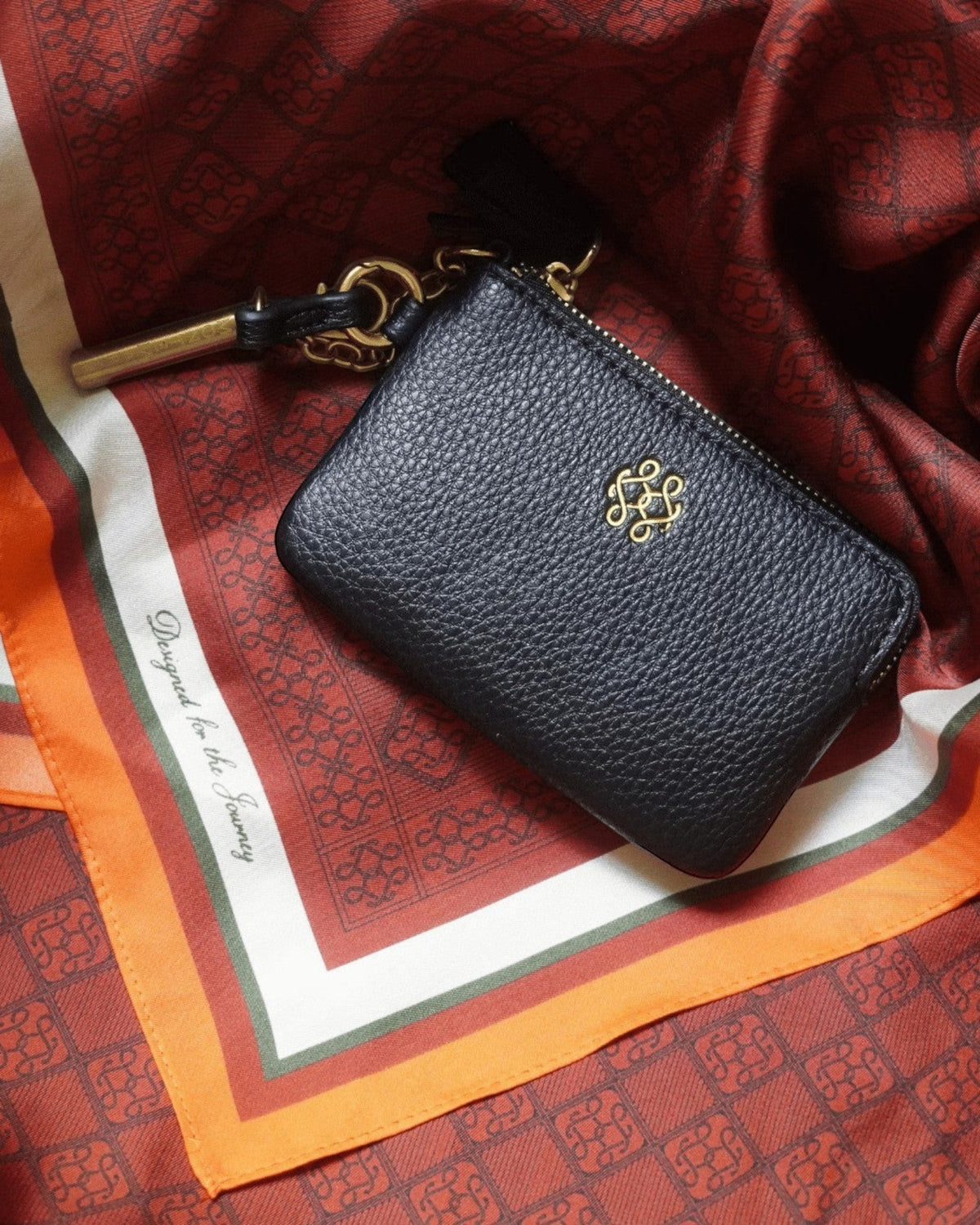 Montemaré black vegan leather RFID card case with a gold logo, zipper closure, and signature orange whistle tassel.