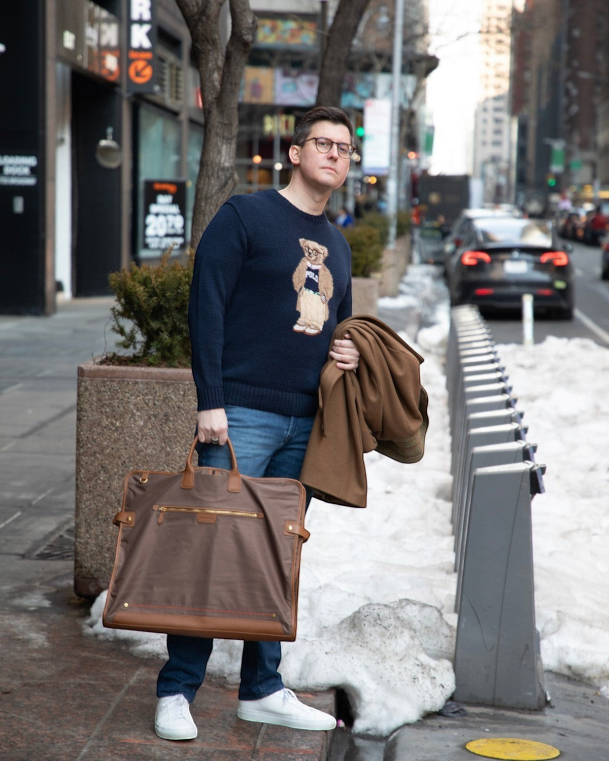 Man holding a brown Montemaré tri-fold garment bag with leather trim while standing on a city sidewalk in winter.