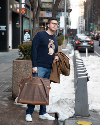 Man holding a brown Montemaré tri-fold garment bag with leather trim while standing on a city sidewalk in winter.