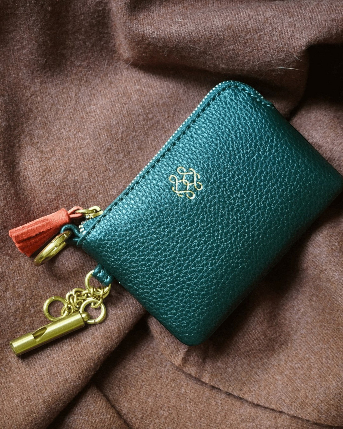 Montemaré green vegan leather RFID card case with a gold logo, zipper closure, and signature orange whistle tassel.