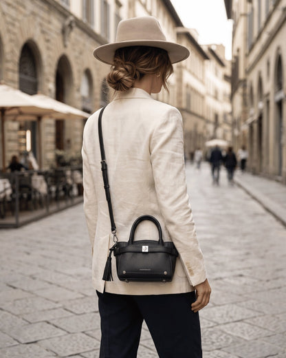 Woman wearing a Montemaré Mayfair Mini Crossbody black leather bag with a tassel detail on a city street