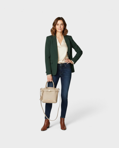 Woman wearing a green blazer and jeans holding a beige Montemaré Mayfair Tall Crossbody bag with tassel detail.