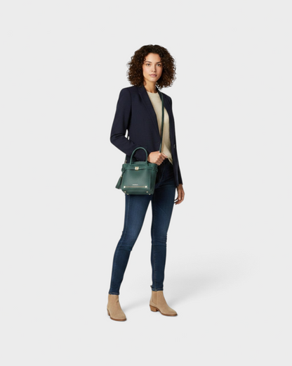 Model wearing a Montemaré Mayfair Tall Crossbody bag in dark green leather with a tassel detail and gold hardware.