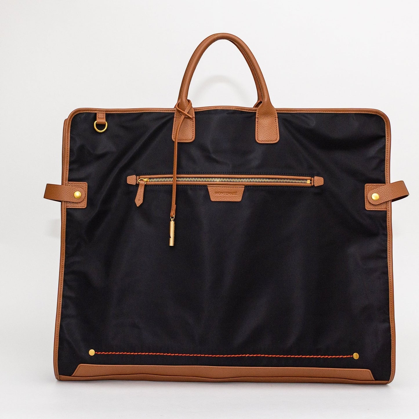 Montemaré Oslo garment bag in black waterproof nylon with tan leather trim, featuring a front zipper pocket and handles.