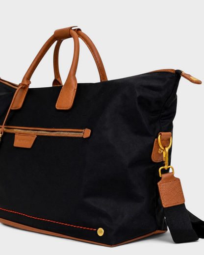 Montemaré Oslo weekender bag in black waterproof nylon with tan leather handles, gold hardware, and shoulder strap.