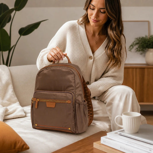 Woman sitting on a sofa holding a brown Montemaré Oslo backpack with leather trim and gold hardware.