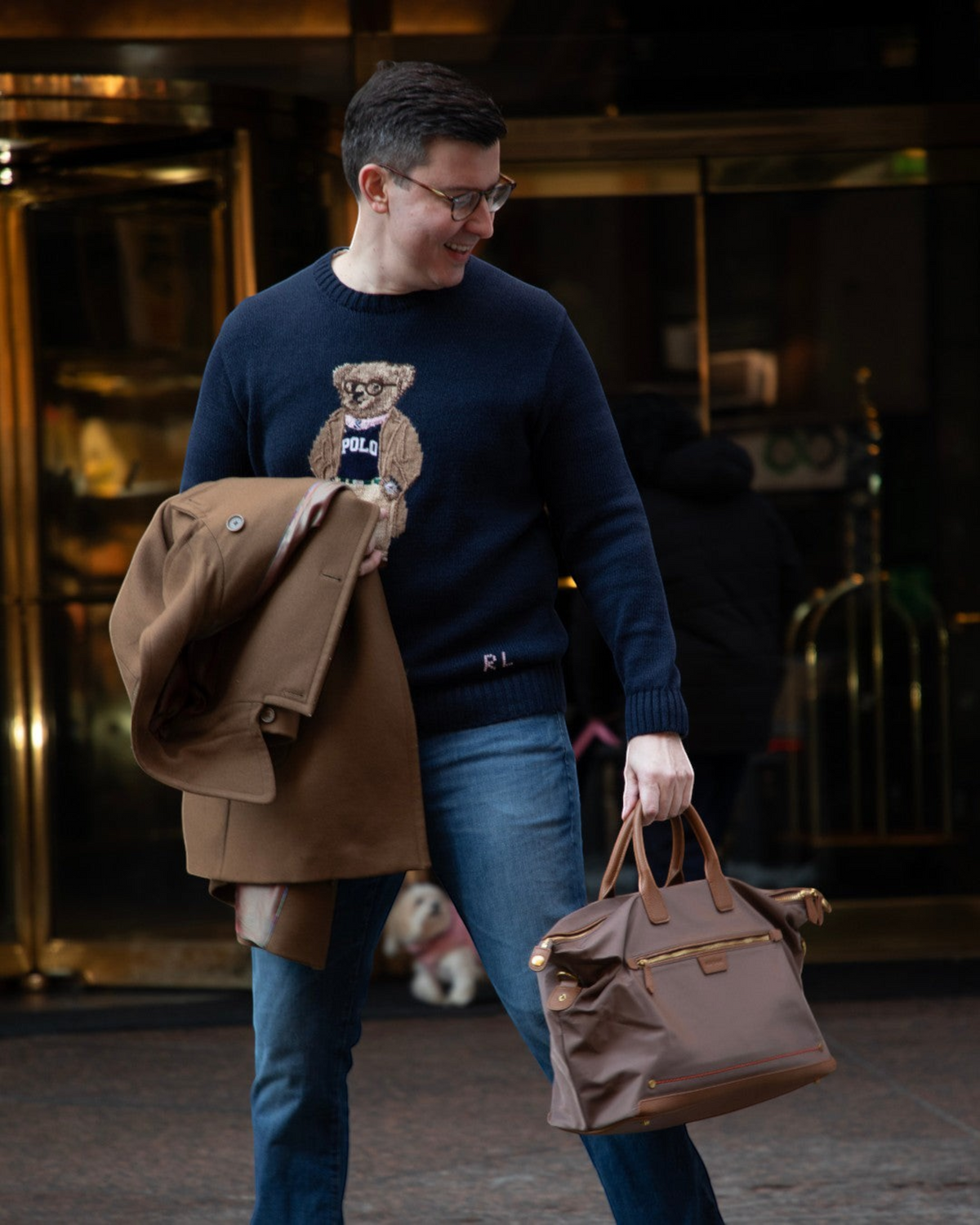 A man carrying a brown Montemaré Oslo RFID-blocking weekender bag with leather trim outside a hotel entrance.