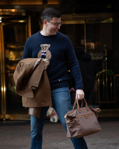A man carrying a brown Montemaré Oslo RFID-blocking weekender bag with leather trim outside a hotel entrance.