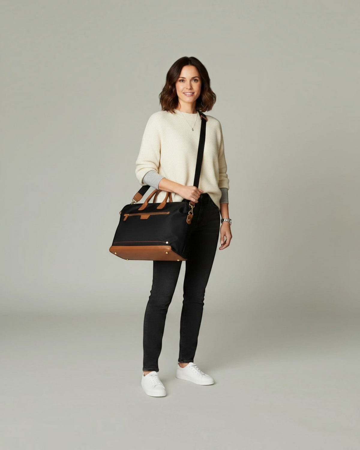 A woman wearing a Montemaré Oslo carry-on bag made of black waterproof nylon with tan leather trim and shoulder strap.