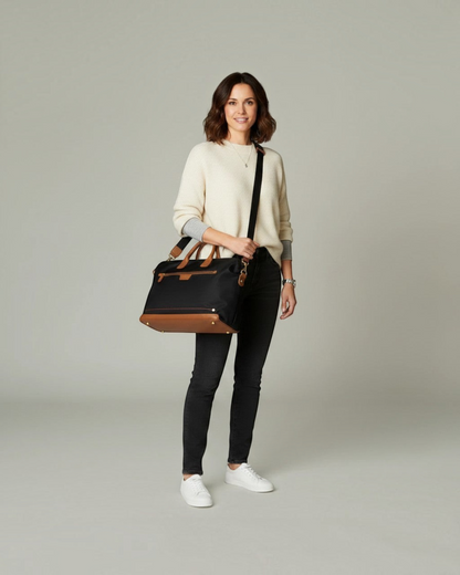 A woman wearing a Montemaré Oslo carry-on bag made of black waterproof nylon with tan leather trim and shoulder strap.