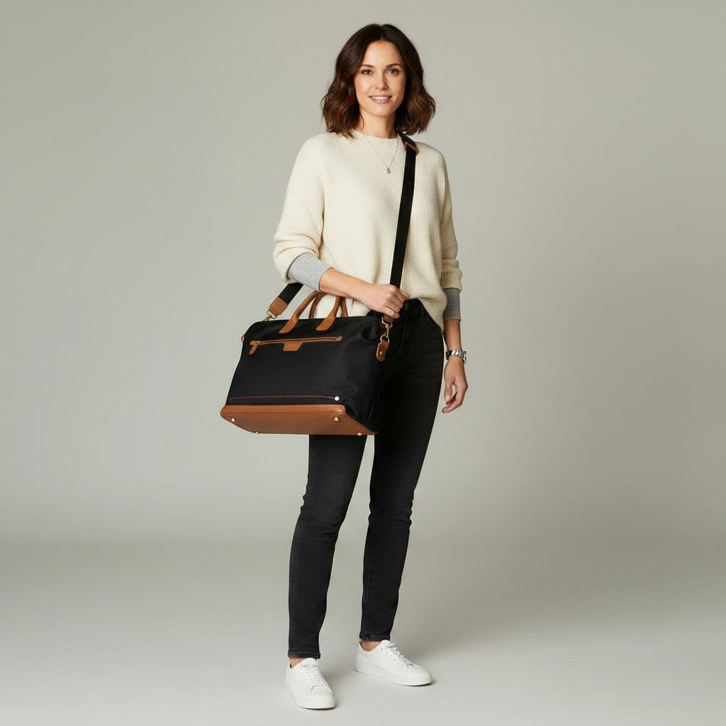 A woman wearing a Montemaré Oslo Carry-On weekender bag made of black waterproof nylon with tan leather accents.