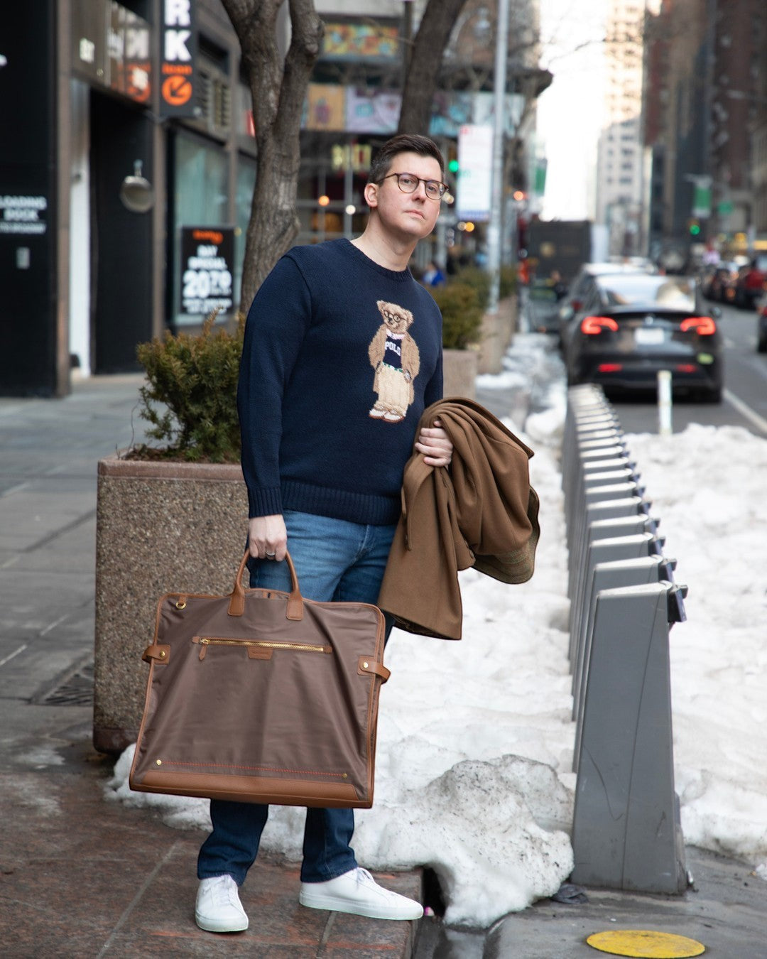Man holding a brown Montemaré Oslo garment bag with leather trim on a city street during winter.