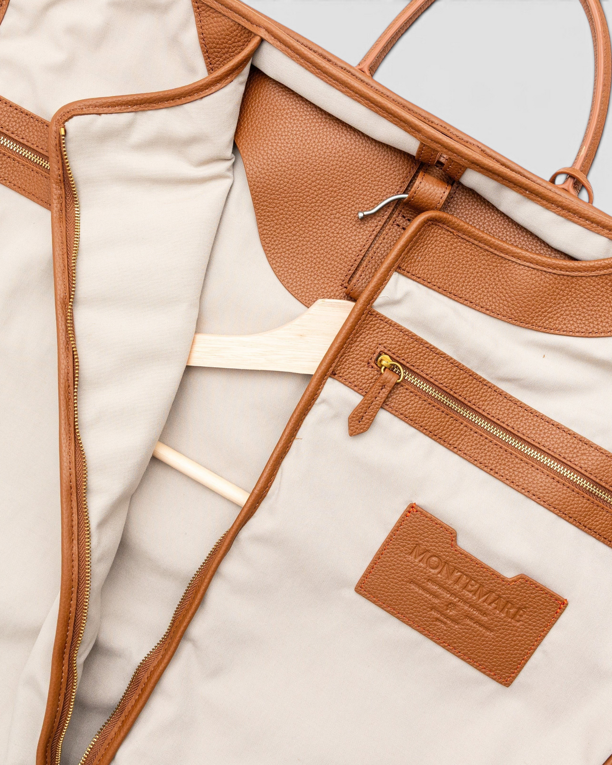 Interior view of a Montemaré Oslo garment bag featuring beige cotton lining, brown leather trim, and a wooden hanger.