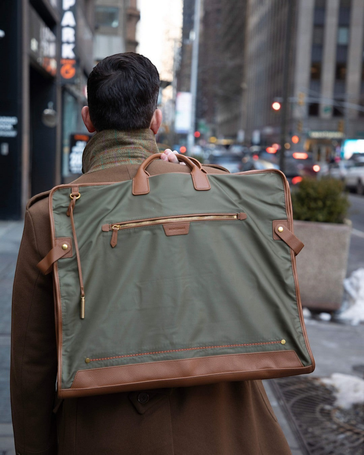 Montemaré Oslo tri-fold garment bag in olive waterproof nylon with brown leather trim carried over a man's shoulder.