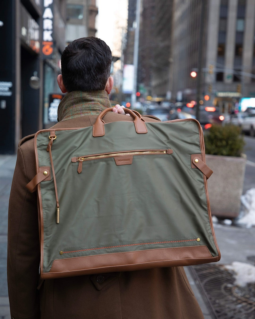 Montemaré Oslo garment bag in olive waterproof nylon with brown leather trim carried on a man's shoulder in the city.