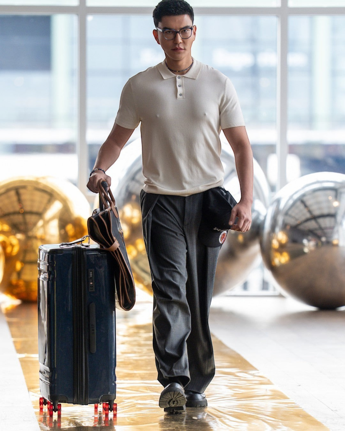 A man walking through a terminal carrying a Montemaré Oslo tri-fold garment bag with leather trim and a suitcase.