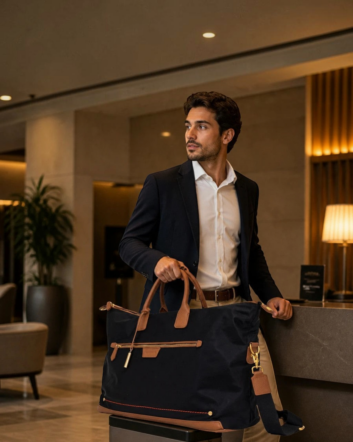 Man in a suit holding a Montemaré Oslo navy nylon and leather weekender bag in a luxury hotel lobby.
