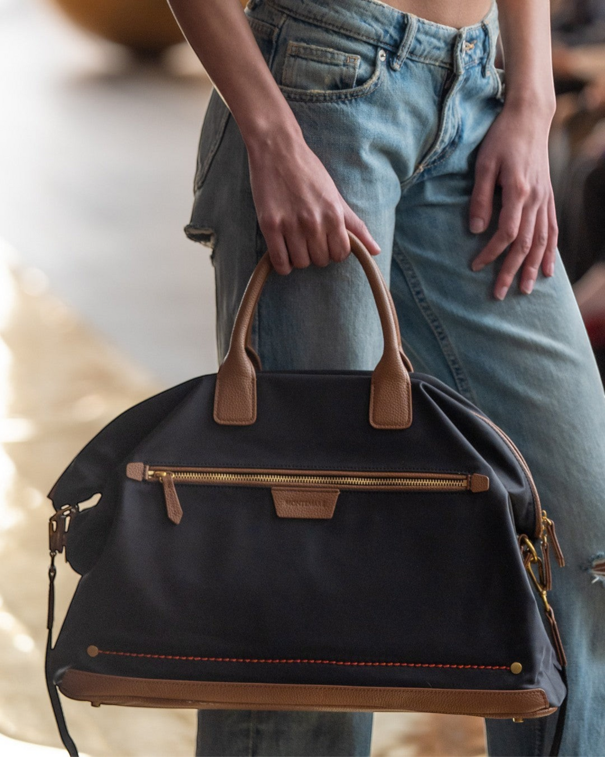 Montemaré Oslo weekender bag in black waterproof nylon with tan leather trim held by a person in denim jeans