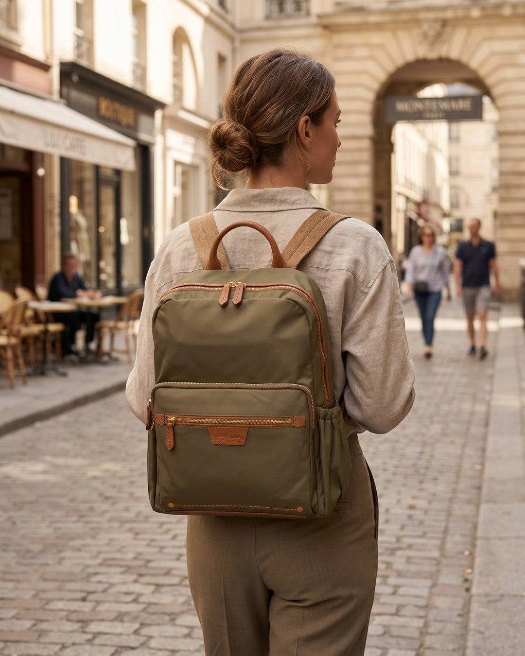 Woman wearing a Montemaré olive green nylon and leather Oslo backpack while walking down a city street.