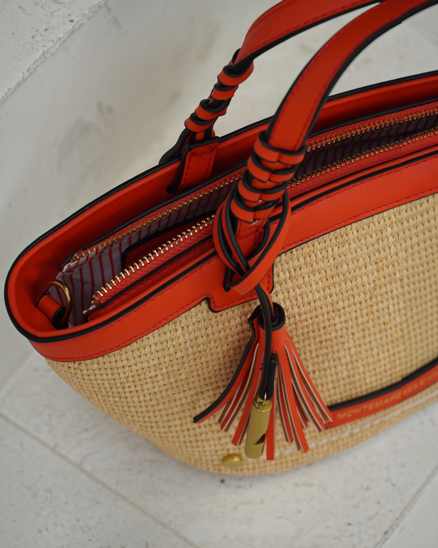 Montemaré Palma Crossbody bag in straw-like material with orange vegan leather trim, top handles, and tassel detail.