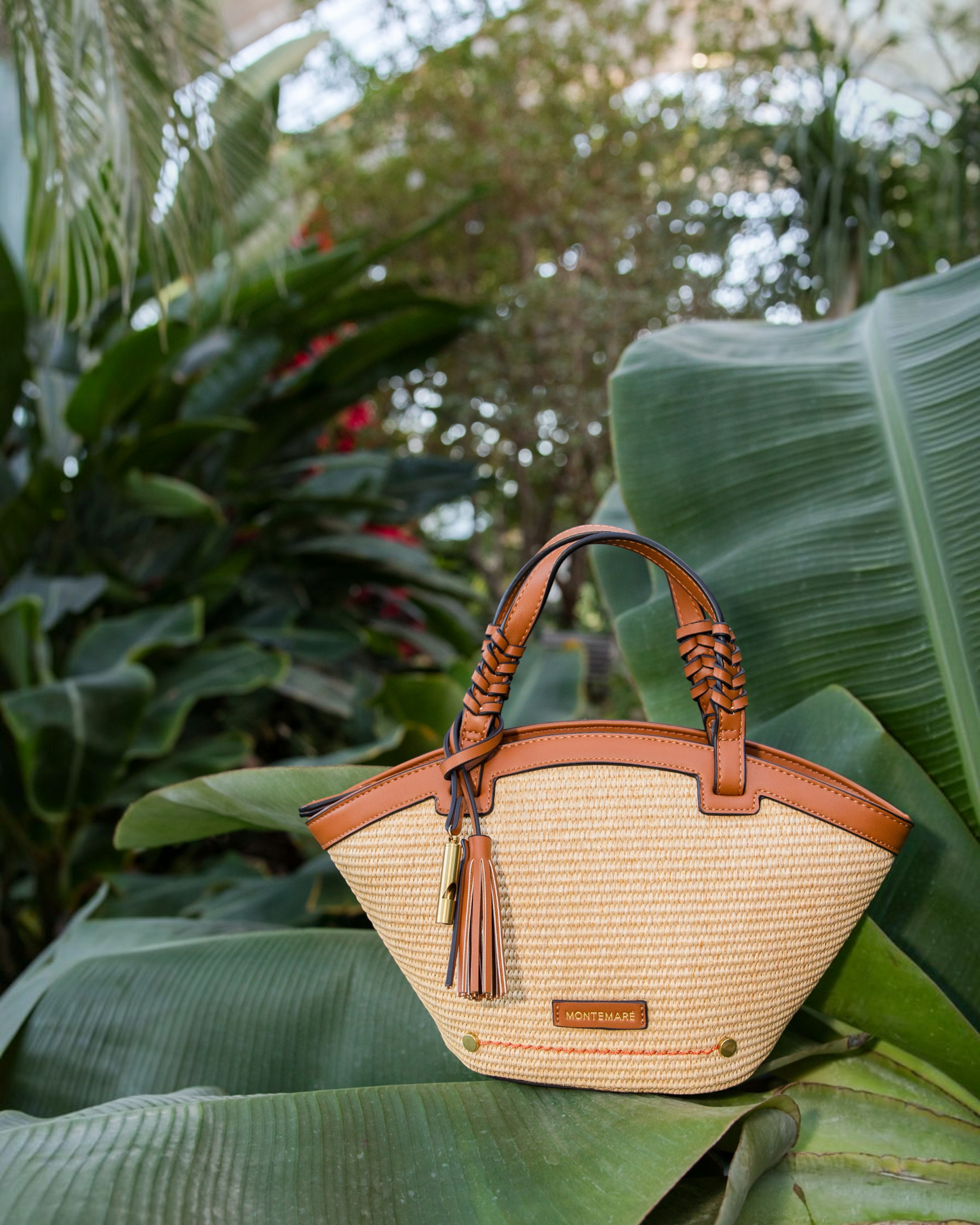 Montemaré Palma Crossbody bag in straw-like material with tan vegan leather trim, top handles, and a tassel charm.