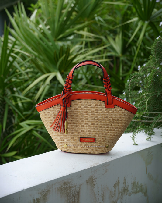Montemaré Palma Crossbody bag in straw-like material with orange vegan leather trim, top handles, and tassel detail.