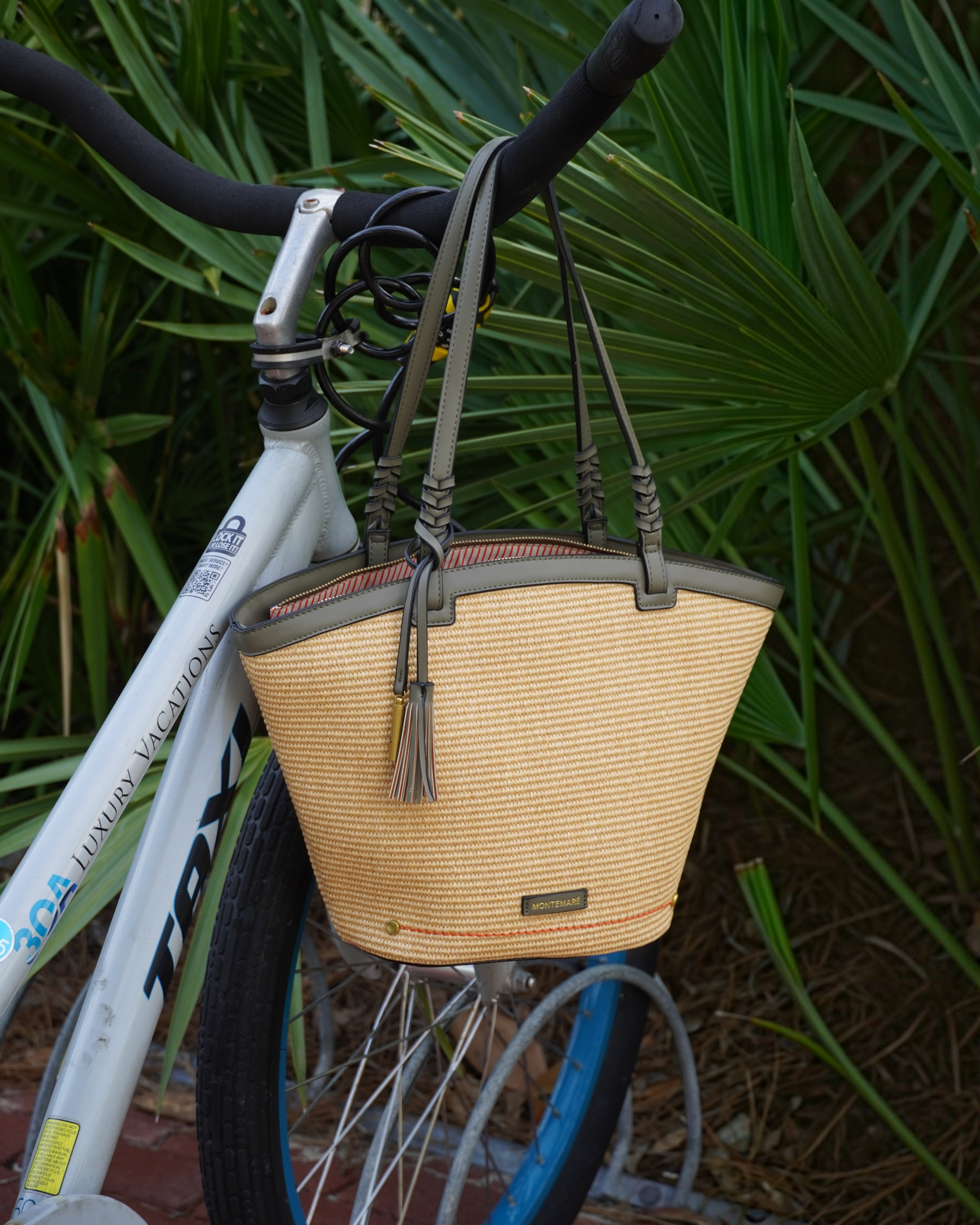 Montemaré Palma straw-style tote bag with olive green vegan leather trim and safety whistle tassel hanging on a bike
