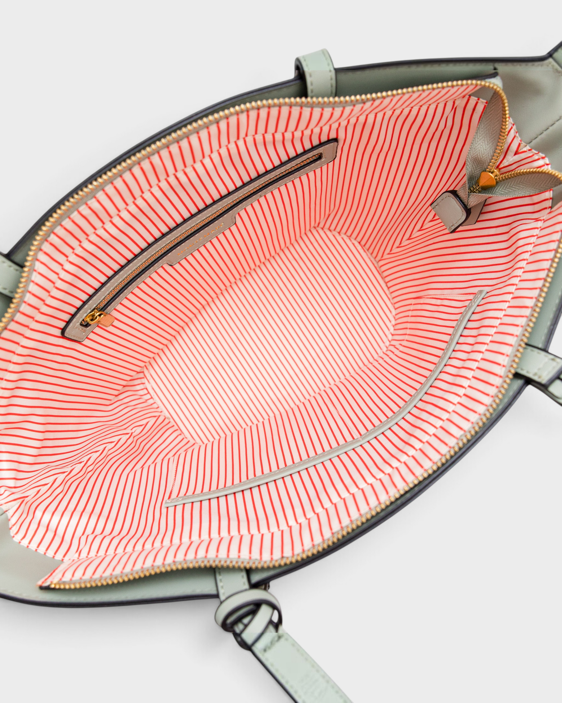 Interior of Montemaré Palma Tote featuring orange and white striped lining, zip pocket, and sage green exterior trim.