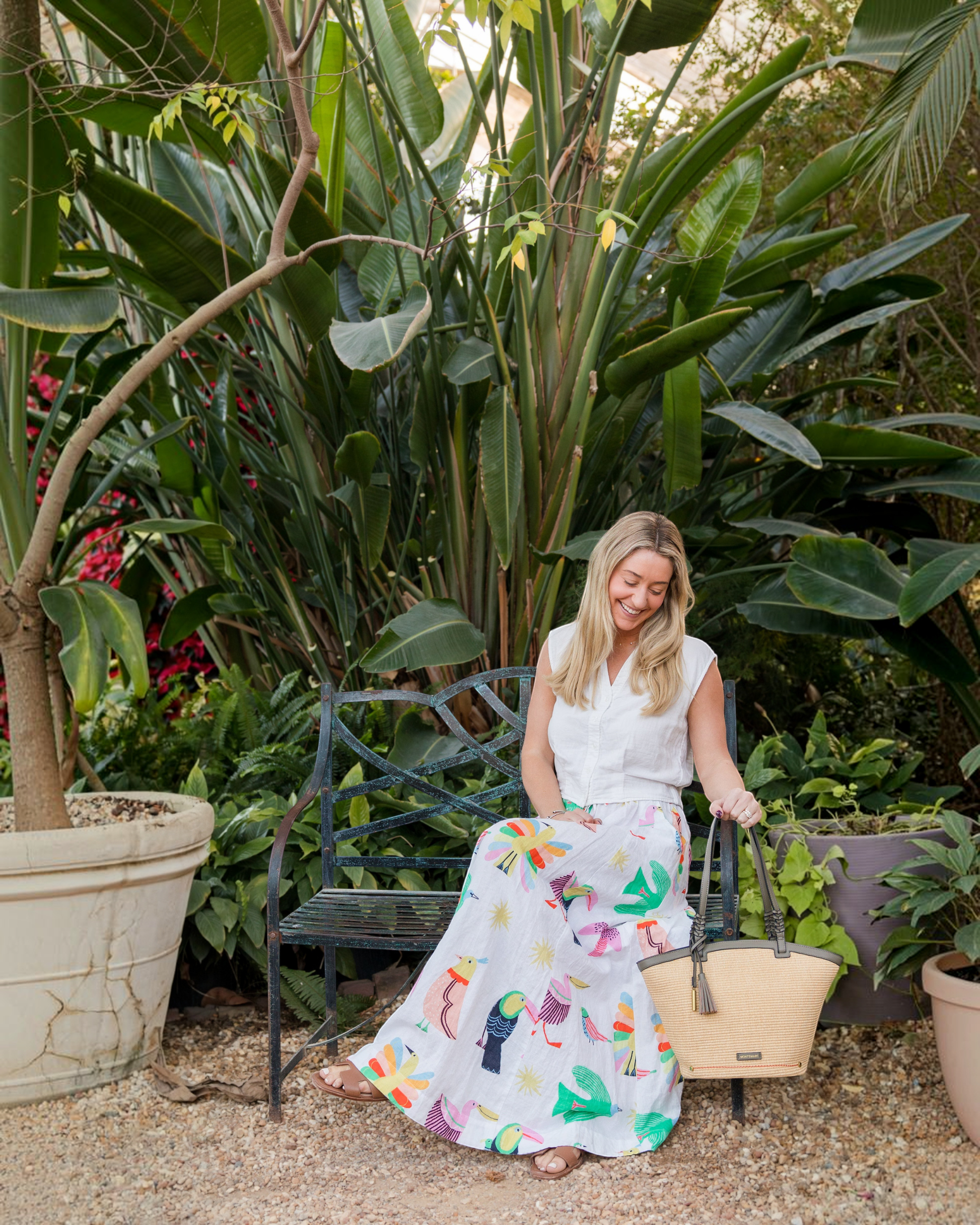 Montemaré Palma Tote in straw-like material with vegan leather trim, held by a woman sitting on a garden bench.