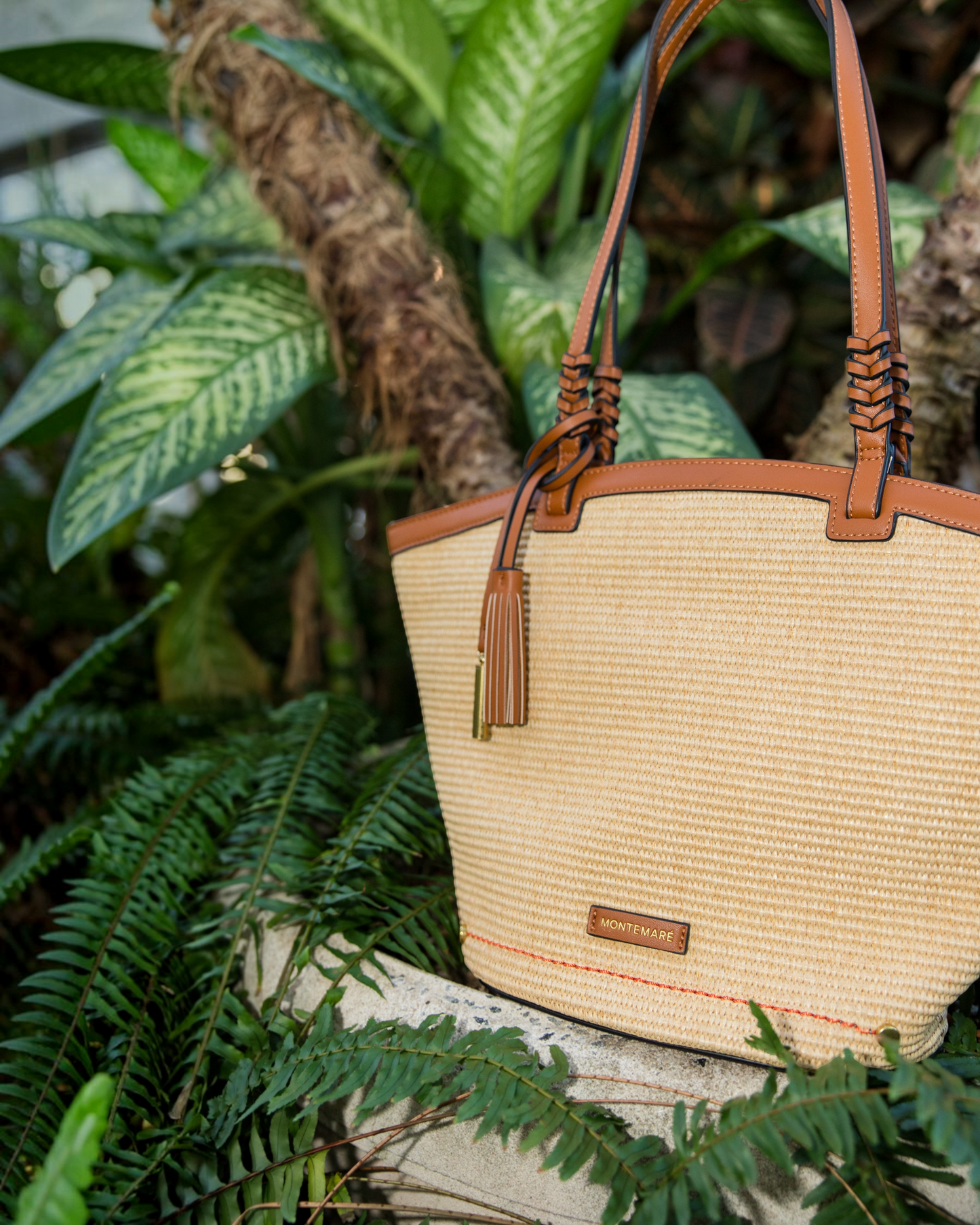 Montemaré Palma Tote in straw-like material with tan vegan leather trim and a signature safety whistle tassel.