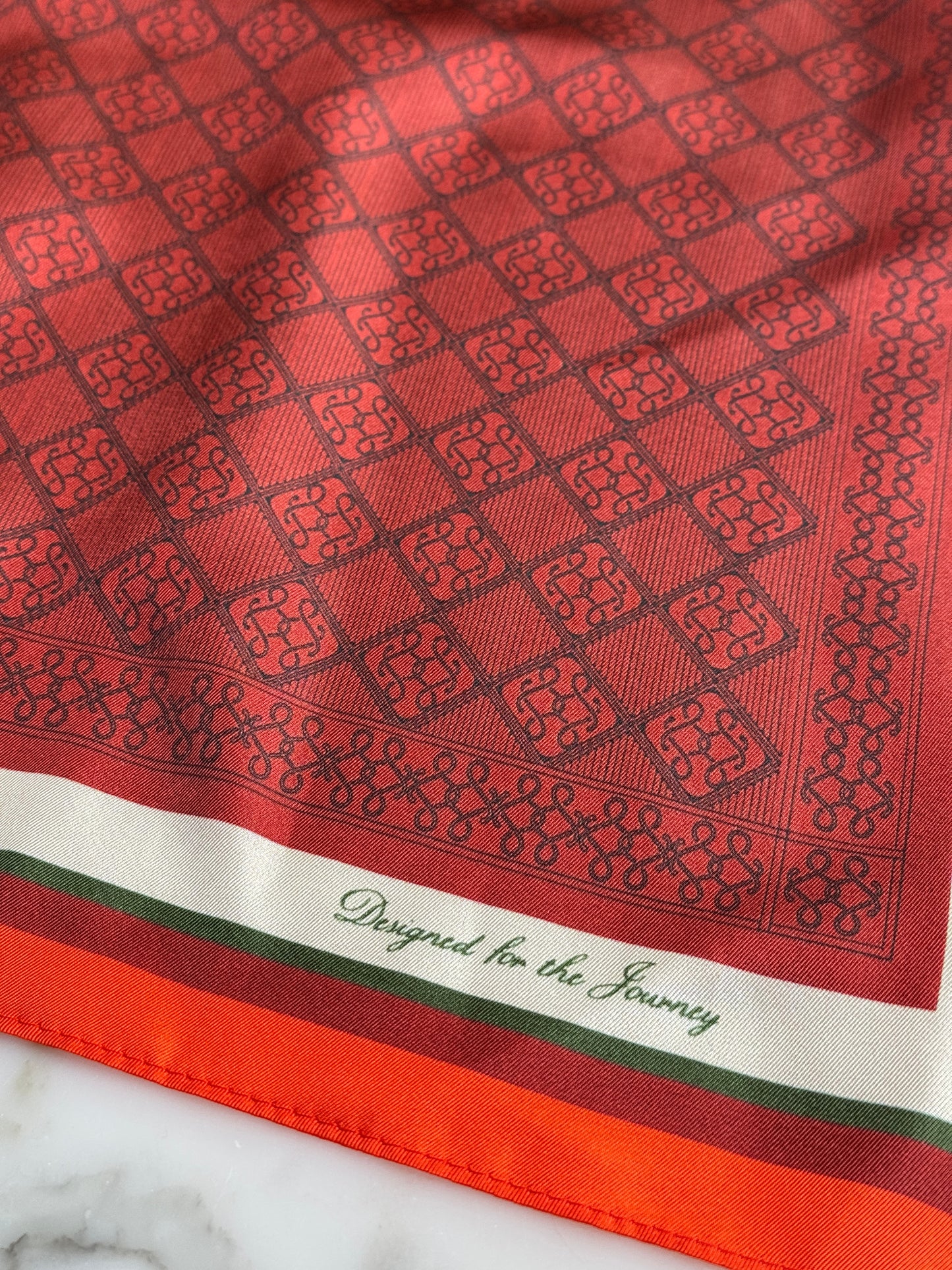 Montemaré red silk square scarf featuring a geometric pattern and a border with the text Designed for the Journey