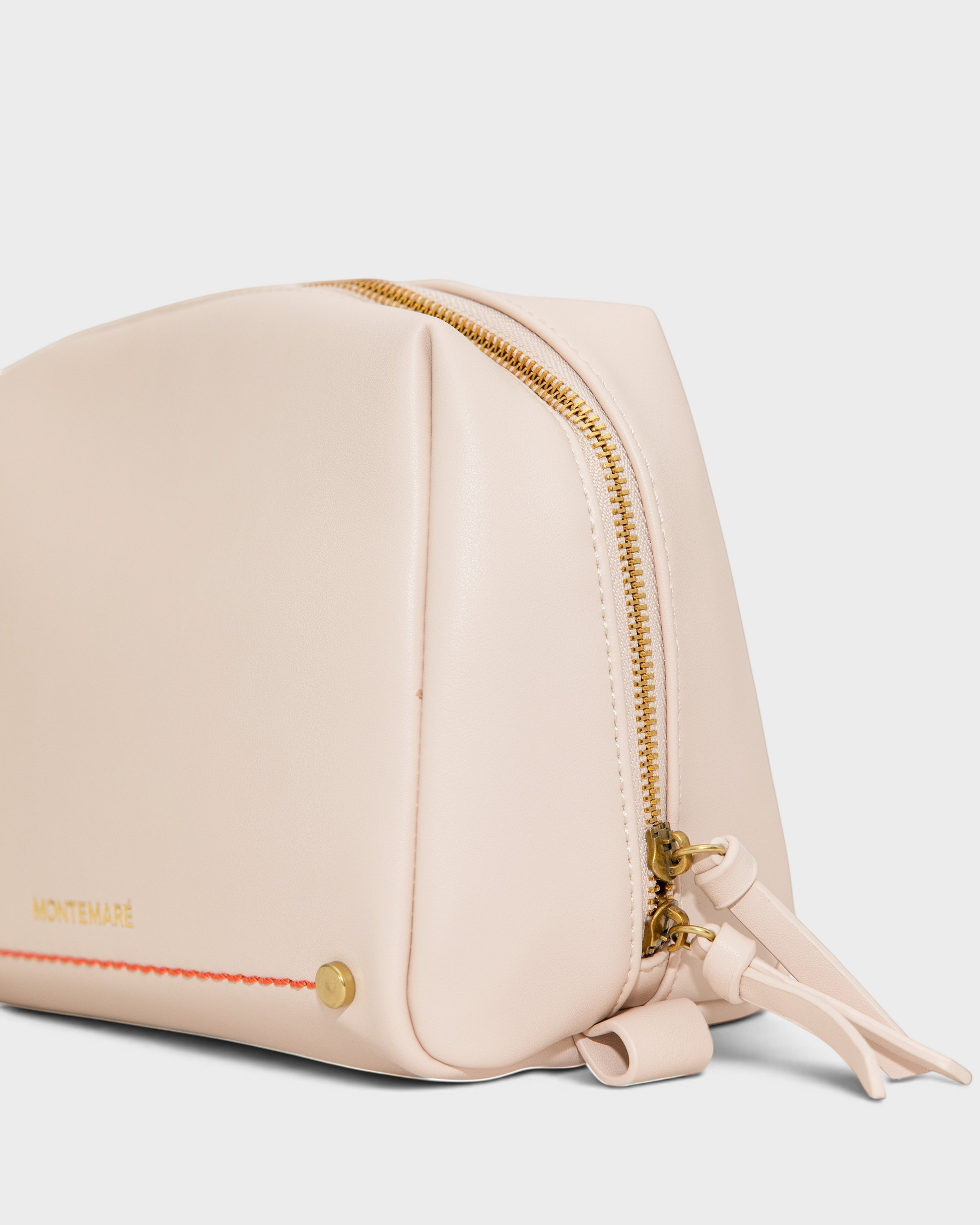 Montemaré Roma standing toiletry case in light beige vegan leather with gold zipper and orange accent stitching.