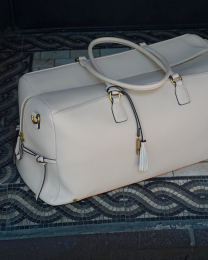Montemaré Roma vegan leather duffel bag in cream with gold hardware, tassel detail, and orange interior trim.