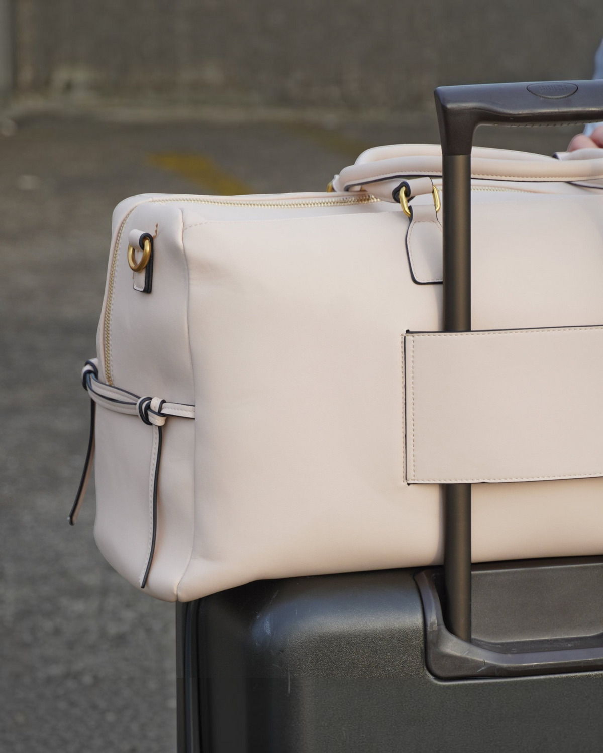 Montemaré Roma Duffel in beige vegan leather attached to a rolling suitcase handle via its integrated trolley sleeve