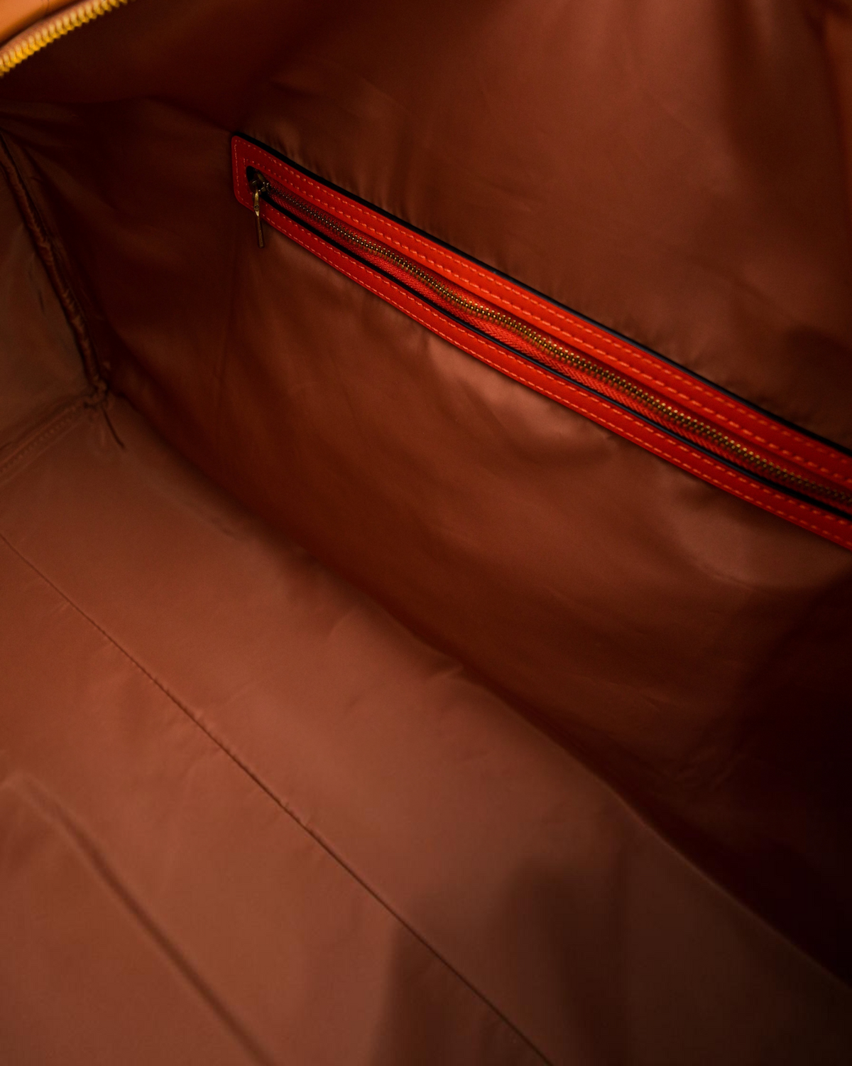 Interior of Montemaré Roma Duffel featuring water-resistant brown lining and a zippered pocket with orange trim