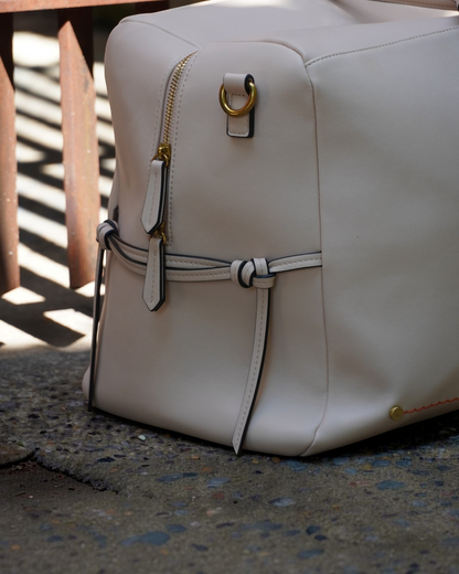 Montemaré Roma Duffel in off-white vegan leather with gold hardware, side view showing zipper and knotted detail