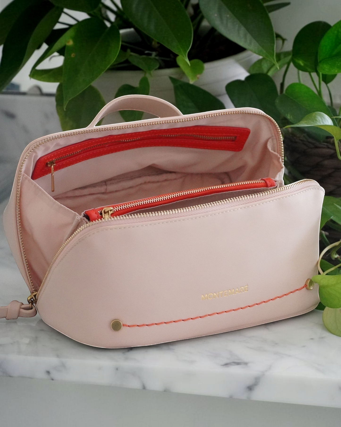 Montemaré Roma foldout toiletry case in blush pink vegan leather with orange accents and a wide zippered opening.