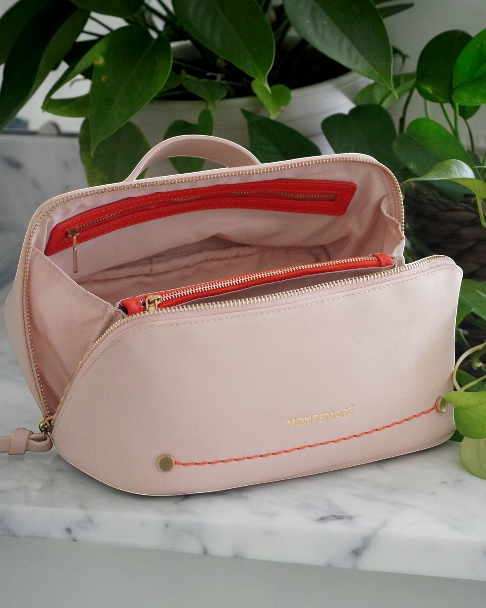 Montemaré Roma foldout toiletry case in blush pink vegan leather with orange accents and a wide zippered opening.