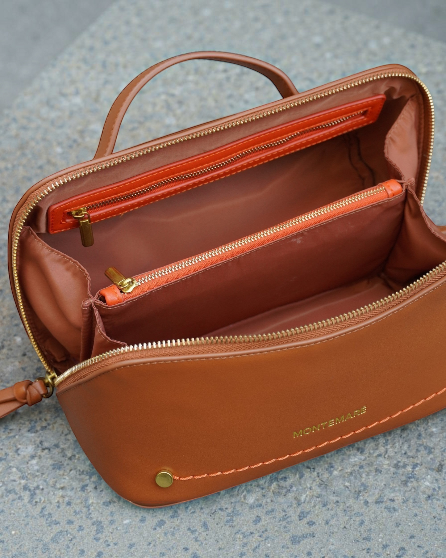 Montemaré Roma foldout toiletry case in brown vegan leather with orange accents, top handle, and zippered interior.